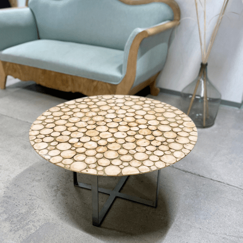 Cette image représente un intérieur avec un canapé, une décoration d'une dame-jeanne et une table basse ronde faite de rondin et de résine.