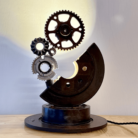 Cette image représente une sculpture faite avec des pièces mécaniques de récupération soudées ensemble et donne l'impression de voir un croissant de lune qui éclaire des planètes.