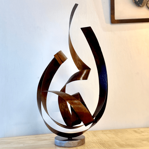 Cette image montre une sculpture faite avec de fines plaques en acier rouillés torsadées et soudées sur un socle rond, elle s'appelle "tout feu tout flamme" car elle donne l'impression de flamme qui s'élève.
