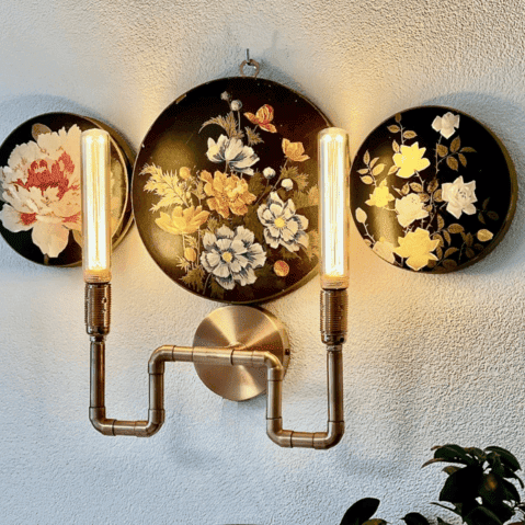 trois anciennes boîtes rondes en carton noir avec des fleurs de couleur transformées en applique mural. la partie électrique est en tube de cuivre rehaussé de deux douille couleur cuivre et ampoules allongées et vintage