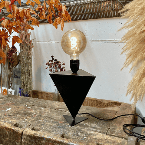 Lampe en métal noir et en forme triangulaire posé sur sa pointe.