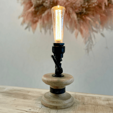 Lampe avec un socle en bois clair rehaussé d'un douille faite avec des raccords sanitaire noir et une ampoule allongée.